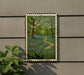 A framed painting depicting a lush forest scene with a winding path and bluebells in the foreground, hanging on a wall.