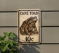 a sign with a drawing of a cane toad, mounted on a wall next to a plant.