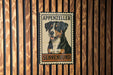 A metal sign with a picture of a dog, mounted on a wooden wall.