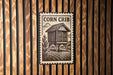 a wooden wall with a metal sign featuring a house and a corn crib.