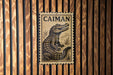 a metal sign with a crocodile illustration on it, mounted on a wooden wall.