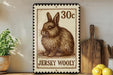 A 30c Jersey Wooly postage stamp is displayed on a wooden shelf, accompanied by a potted plant, a wooden cutting board, and a bunch of lemons.