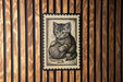 A framed image of a cat sitting on a ball of yarn is displayed on a wooden wall.