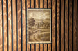 a framed illustration of a rural landscape, depicting a winding road, a tree, and a village in the distance.
