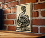 A sign featuring a snake, specifically a Ball Python, is displayed on a brick wall.