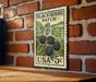 A vintage postage stamp featuring a blackberry patch, mounted on a brick wall.