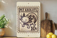 A wooden shelf displaying a wooden cutting board, a potted plant, and a wooden plaque featuring a cartoon axolotl.