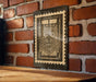 a wooden table with a framed picture of a window with a floral design hanging on the wall behind it.