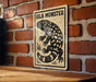 A sign featuring a black and white illustration of a gila monster, a type of lizard, against a brick wall background.