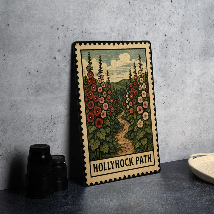 A framed illustration of a floral path, with a vintage-style border, is displayed on a table next to a stack of black camera lenses.