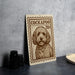 A metal sign featuring a dog illustration, with the text "COCKAPOO 20¢" printed on it, is displayed on a table next to some black camera lenses.