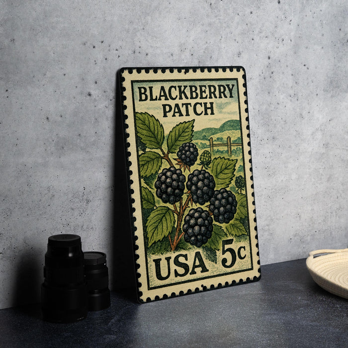 A vintage postage stamp featuring a blackberry patch, placed on a table next to some black camera lenses.