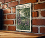 A framed illustration of a forest scene with pink flowers is displayed on a brick wall.