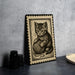 A framed illustration of a kitten sitting with a ball of yarn on a table.