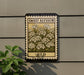 a vintage-style stamp or sign with a floral design, mounted on a wall next to a plant.