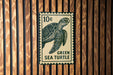 A green sea turtle stamp is displayed on a wooden wall.