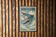A vintage-style metal sign with the text "HANG GLIDING" and an illustration of a person hang gliding against a cloudy sky background.