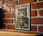 A metal stamp featuring a cat's face is mounted on a brick wall.