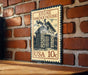 A vintage-style metal sign with a brick wall backdrop, featuring an illustration of a brick house and the text "STONE SMOKEHOUSE" and "USA 10c".