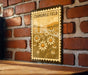 A framed illustration of a field of white flowers is hanging on a brick wall.