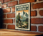 A vintage-style metal sign with a hiker and mountain landscape, mounted on a brick wall.