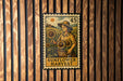 A metal stamp with a woman holding a basket of sunflowers, set against a wooden background.