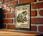A metal sign with a frog illustration is mounted on a brick wall.