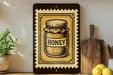 a framed illustration of a jar of honey on a shelf, with a wooden cutting board and a potted plant nearby.
