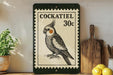 a decorative sign with a bird illustration, placed on a shelf next to a wooden cutting board and some lemons.