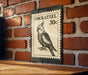 A vintage-style postage stamp featuring a detailed illustration of a cockatoo, with the text "COCKATIEL 30c" printed on it. The stamp is mounted on a brick wall, and there is a wooden table below it.