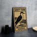 A metal sign with a bird illustration and text, placed on a table next to some black camera lenses.