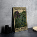 A metal sign with a postage stamp design, featuring an illustration of iris pond flowers and lily pads, placed on a table next to some black camera lenses.