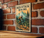 A vintage-style metal sign with a mountain landscape and a person riding a bicycle, mounted on a brick wall.