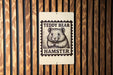 A metal sign with a teddy bear image and the text "Teddy Bear Hamster" is mounted on a wooden wall.