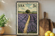 A framed illustration of a lavender field with a path leading through it, displayed on a shelf next to a wooden cutting board and a potted plant.
