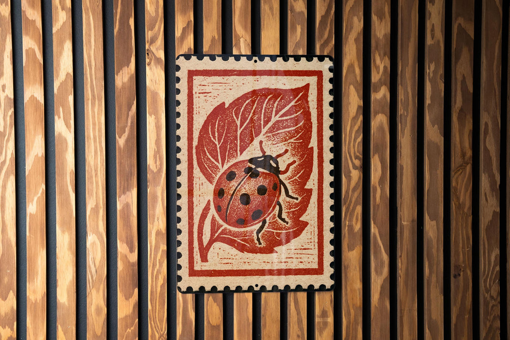 A red and white postage stamp featuring a ladybug on a leaf is displayed against a wooden background.