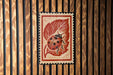 A red and white postage stamp featuring a ladybug on a leaf is displayed against a wooden background.