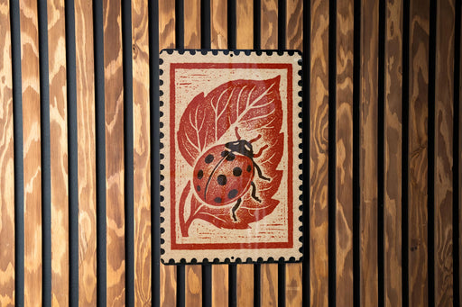 A red and white postage stamp featuring a ladybug on a leaf is displayed against a wooden background.
