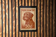 A wooden wall with a brown wooden slat pattern. On the wall, there is a brown and white postage stamp featuring a dog's head.