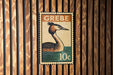 A postage stamp featuring a bird, likely a crane, is displayed on a wooden wall.