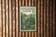 A vintage-style postage stamp featuring a garden scene with a watering can and a wooden barrel, mounted on a wooden wall.