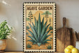 a framed illustration of an agave plant, with the text "AGAVE GARDEN" prominently displayed. The frame is placed on a wooden surface, with a potted plant to the left and a wooden cutting board to the right.