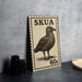 a black and white stamp-like object with a bird illustration, placed on a dark surface next to some black camera lenses.