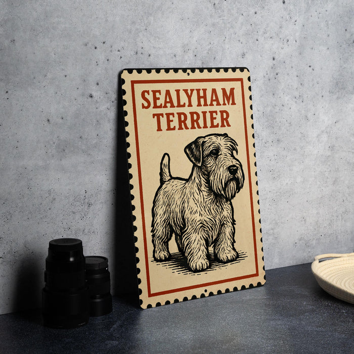 A metal sign with a picture of a Sealyham Terrier dog on it, placed on a countertop next to some black camera lenses.