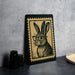 A framed illustration of a rabbit wearing glasses is displayed on a table, accompanied by a stack of black camera lenses and a woven basket.