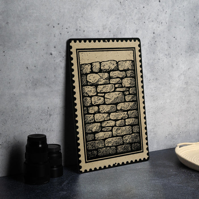 a framed illustration of a brick wall, placed on a dark surface next to a stack of black camera lenses.