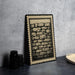 a framed illustration of a brick wall, placed on a dark surface next to a stack of black camera lenses.