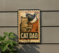 A sign with a cat and the word "CAT DAD" printed on it, mounted on a wall next to a plant.