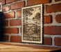 A metal sign with a vintage-style illustration of a wooden gate and a field, mounted on a brick wall.
