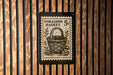 A black and white postage stamp featuring a basket and mushrooms, mounted on a wooden wall.